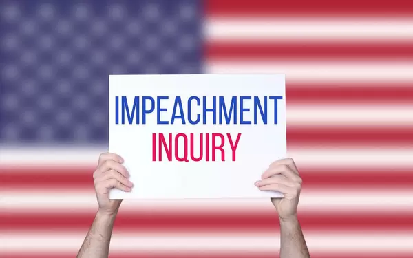 Hands holding board with Impeachment Inquiry text with USA flag background.jpg