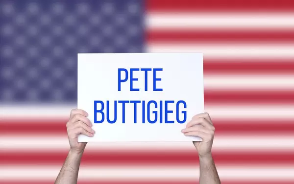 Hands holding board with Pete Buttigieg text with USA flag background
