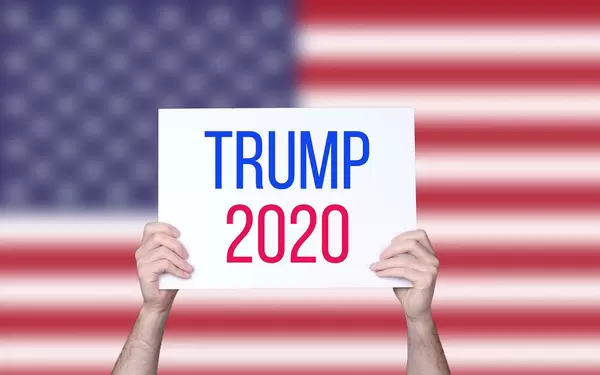 Hands holding board with Trump 2020 text with USA flag background