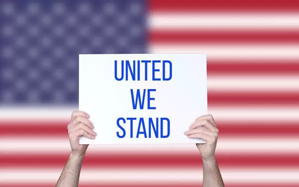 Hands holding board with United we stand text with USA flag background.jpg