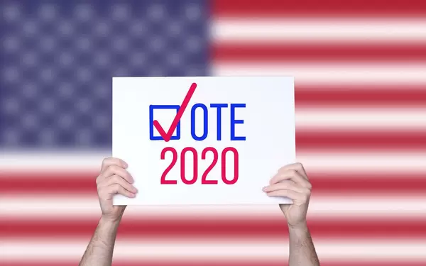 Hands holding board with Vote 2020 concept with USA flag background