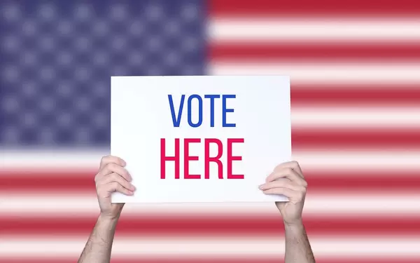 Hands holding board with Vote here text with USA flag background.jpg