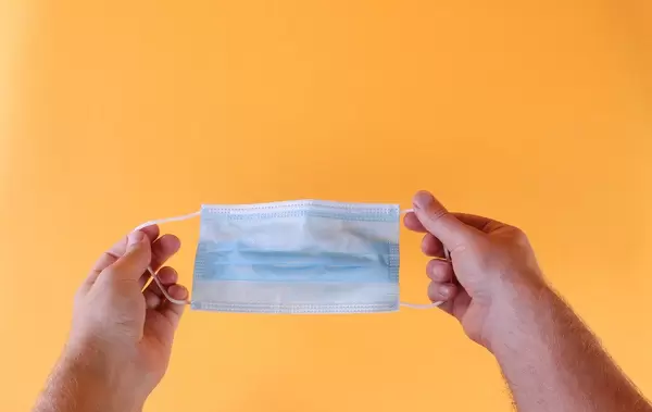 Hands holding medical face mask on orange background