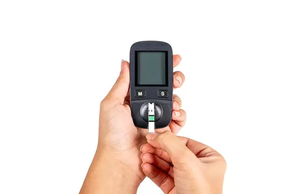 Hands holds blood glucose meter with test strip on white background