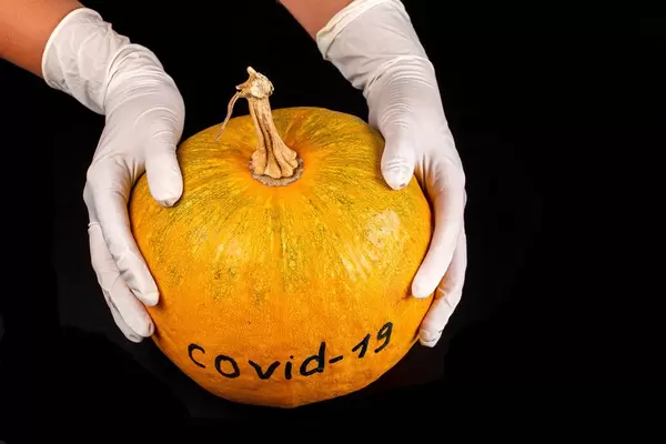 Hands in gloves hold an orange pumpkin with the inscription Covid-19 on a black background