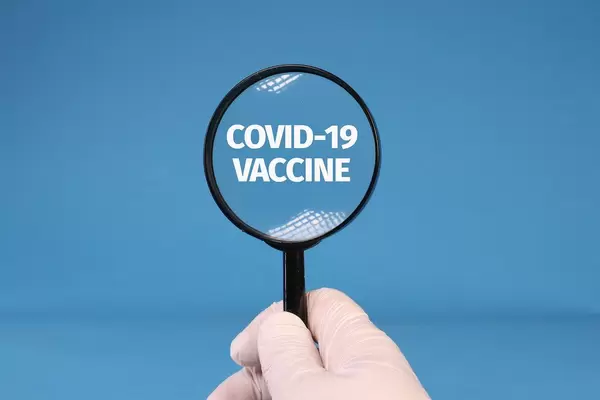 Hands in medical gloves holding magnifying glass over Covid-19 Vaccine text