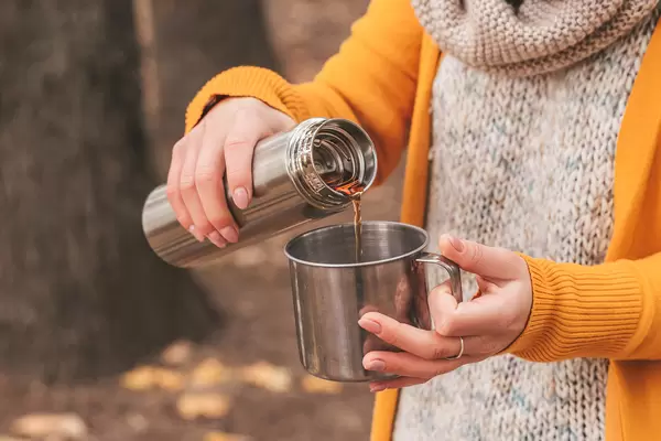 Hands of a girl pour tea from a thermos into a mug on an autumn background