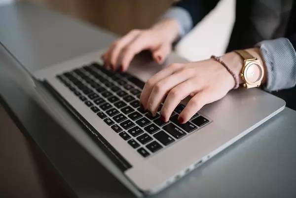 Hands of a woman in business attire typing on a Macbook keyboard