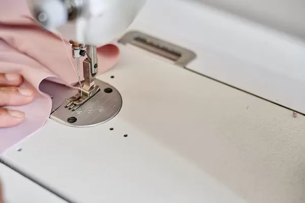 Hands of a young woman sew on a white sewing machine