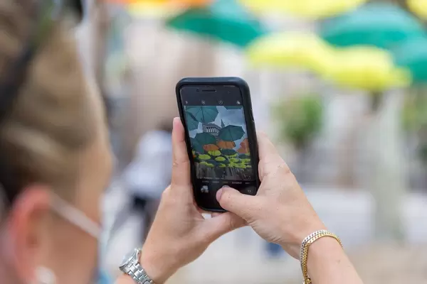 Hands of tourist with face mask taking an iPhone photo of multicoloured umbrellas in Sóller, Majorca