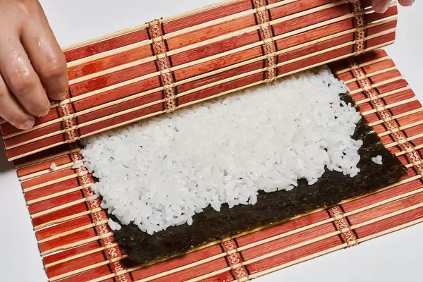 Hands of woman chef filling japanese sushi rolls with rice on a nori seaweed sheet