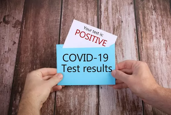 Hands opening blue envelope with Positive Covid-19 results