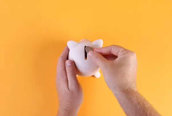 Hands putting coin into piggy bank on oragne background