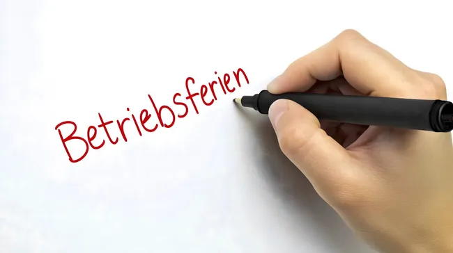 Handschriftlicher Schriftzug 'Betriebsferien' auf weißer Tafel