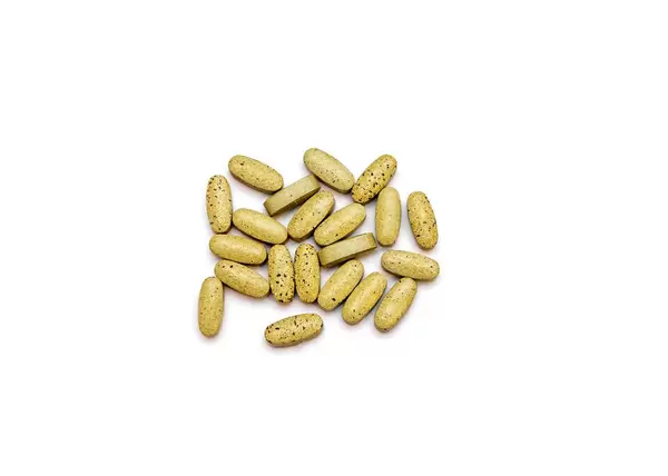 Handvoll gelbe Vitamintabletten vor weißem Hintergrund