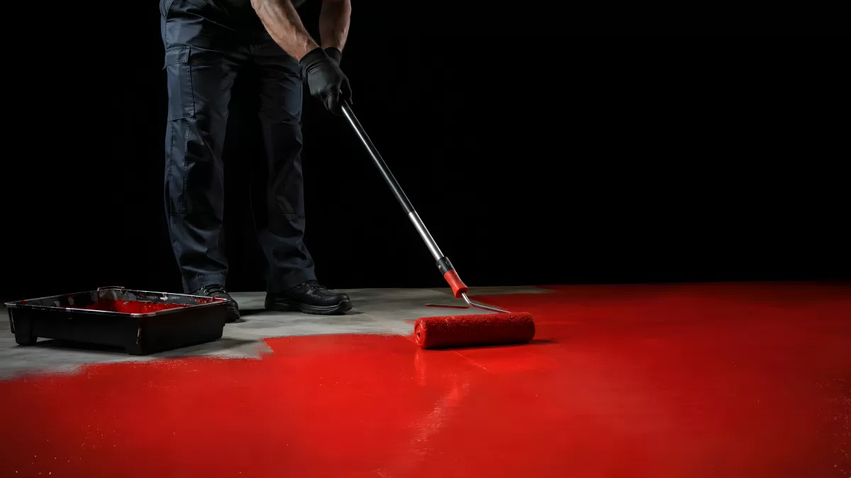 Handwerker streicht Betonboden mit roter Farbe