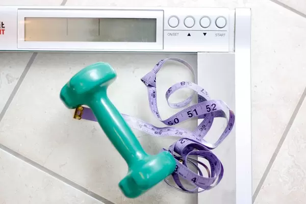 Hantel und Maßband auf einer Waage