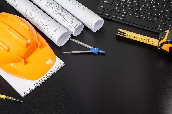 Hard hat, notepad, rolls of drawings on a black background with a keyboard and a compass, the concept of engineering or design work