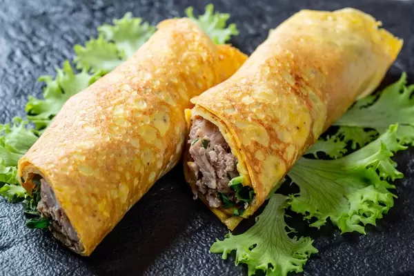 Hausgemachte Eieromelette gerollt und gefüllt mit Fleisch und Kräutern auf Salatblatt