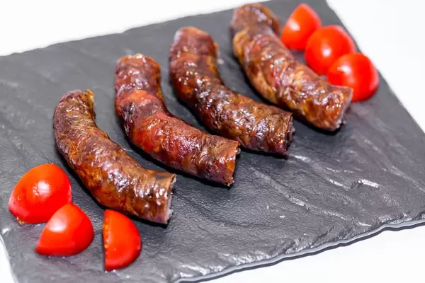 Hausgemachte, gebratene Wurst mit geschnittenen Tomaten auf schwarzer Platte