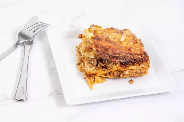 Hausgemachte Lasagne auf einem quadratischen Teller, mit Besteck, auf einer Marmoroberfläche