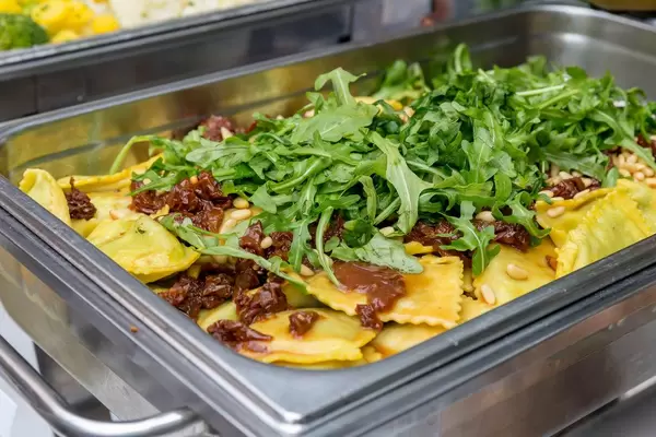 Hausgemachte Ravioli mit Spinat gefüllt, dazu getrocknete Tomaten Pinienkerne und Rucola an einem Buffet