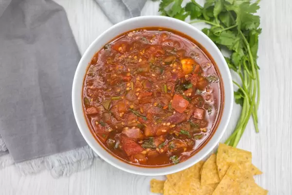 Hausgemachte Salsa mit Tomaten, Zwiebeln und Gewürzen neben Bund Petersilie und Nachos