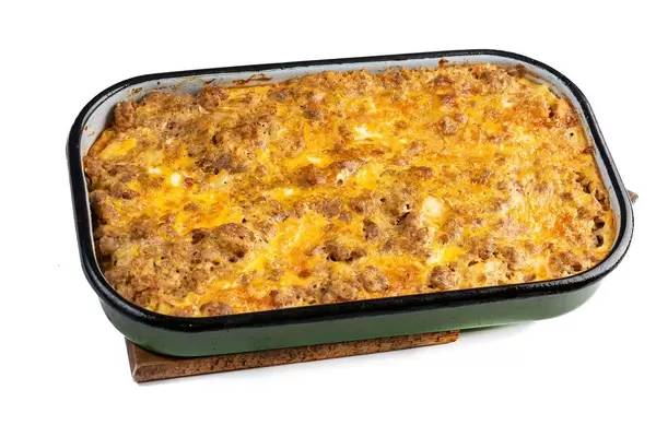 Hausgemachter Hackfleisch-Kartoffel-Auflauf mit Käse überbacken, in grüner Auflaufschale auf weißem Untergrund