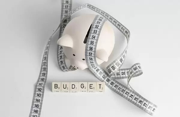 Haushaltsplan: Sparschwein mit Maßband und Buchstabenwürfeln welche das Wort 'Budget' schreiben - Draufsicht mit weißen Untergrund