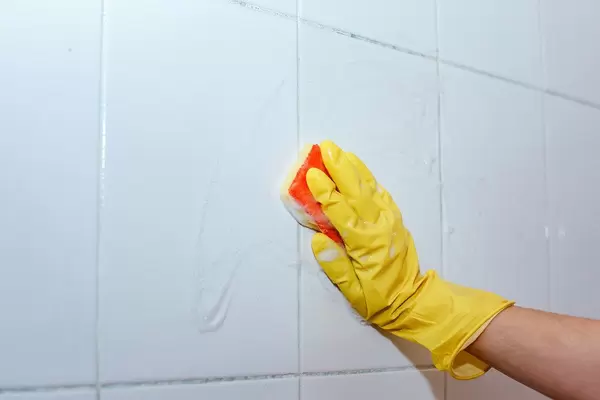 Hausmädchen reinigt die Badezimmer-Fliesen mit einem Schwamm und Latexhandschuhen