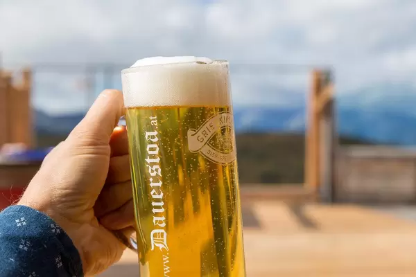Having a beer in the mountains: hand holding glass of beer with foam on the terrace of Dauerstoa hut