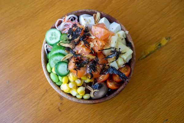 Hawaiianische Poke Bowl mit frischem Gemüse, Tofu, Wachteleier, Lachs, Röstzwiebeln und getrockneter Seetang in einer Holzschüssel Draufsicht