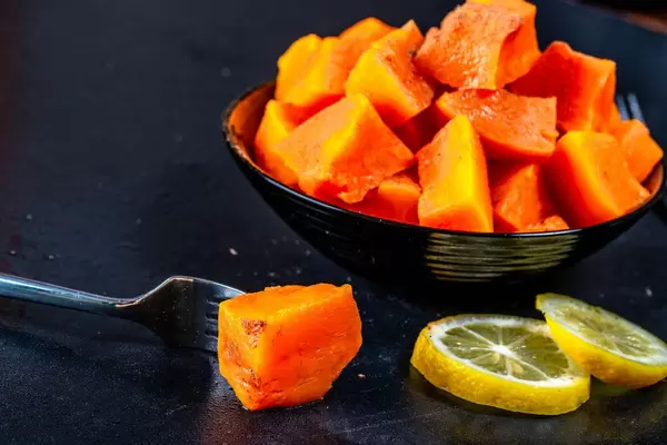 Healthy baked pumpkin dessert with lemon slices and fork on black background