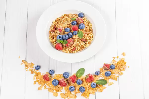Healthy breakfast background with cereal flakes, strawberries, blueberries and mint on a white wooden table