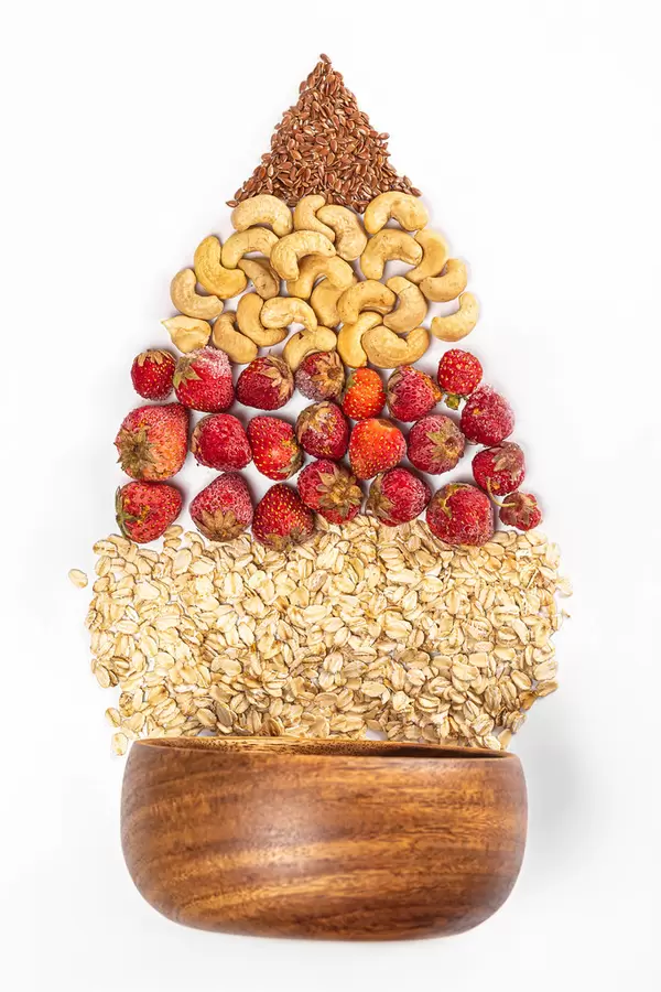 Healthy breakfast - bowl with oatmeal, strawberries, cashews and flax seeds on white