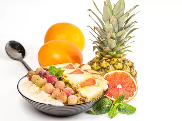 Healthy food concept - porridge with fresh fruits, berries and nuts on white background with pineapple, grapefruit and mint