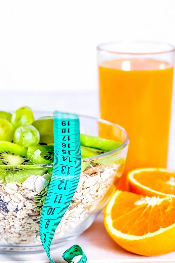 Healthy food: fresh orange juice, an orange cut in pieces, a bowl with muesli, kiwi and grapes and a measuring tape