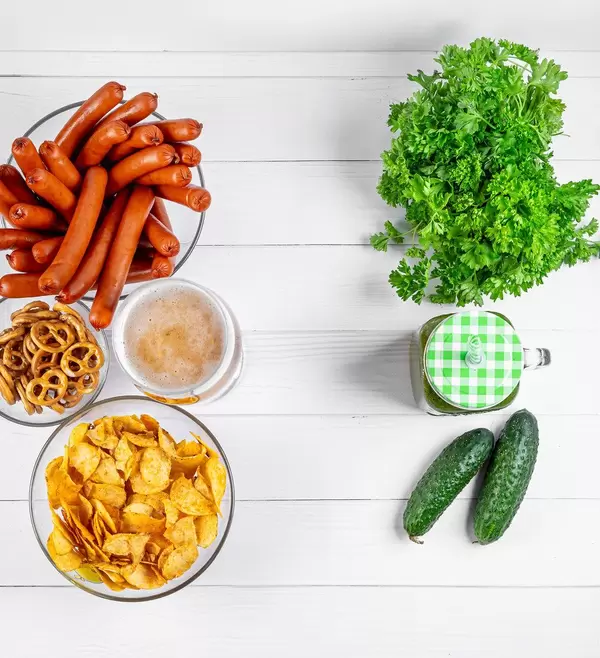 Healthy foods on one side, and beer with chips and sausages on the other, top view. Healthy and unhealthy diet