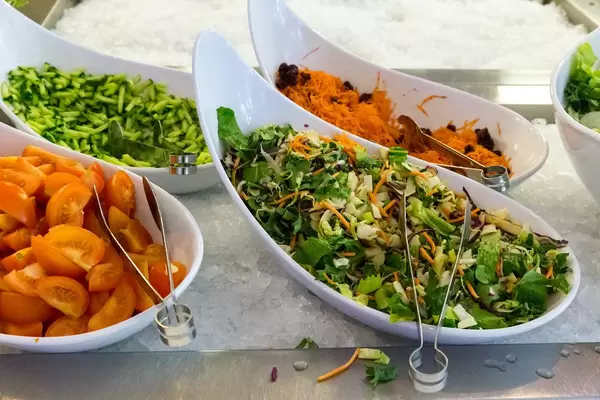 Healthy lunch with salad, grated carrots, cucumbers and tomatoes in curved bowls on refrigerated containers filled with crushed-ice