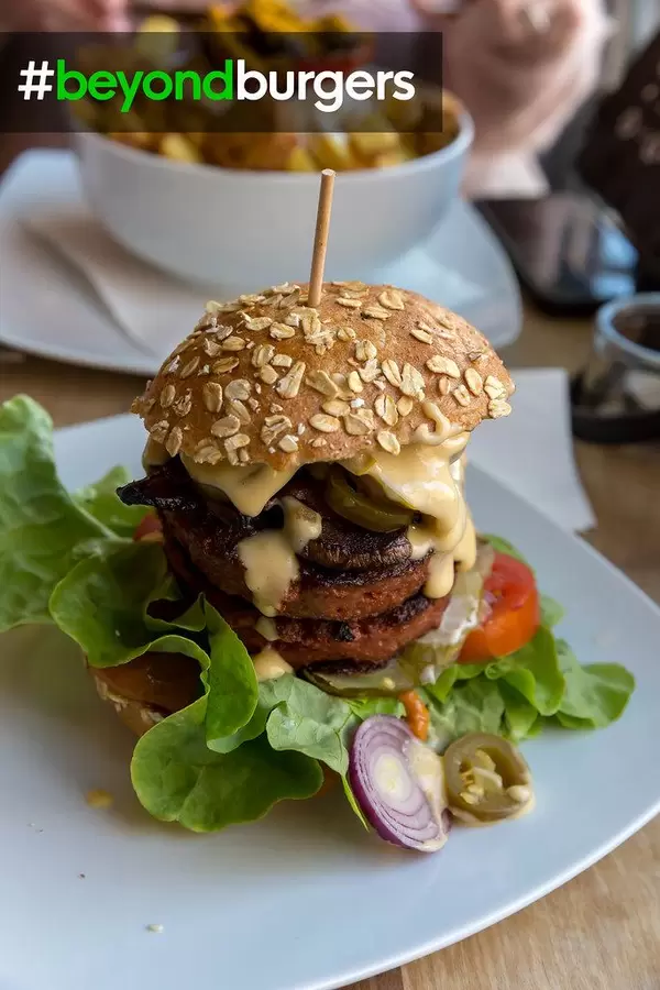 Healthy soy-free and gluten-free burger by Beyond Meat Burger, for a vegan diet, served in a burger roll, with sauce, salad, cucumber, tomatoes and onions
