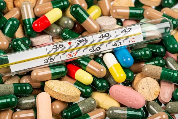 Heap of medical capsules, tablets and thermometer