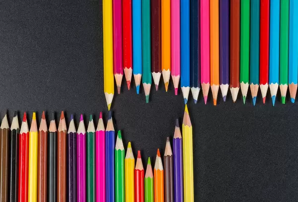 Heart laid out of colored pencils on a black background