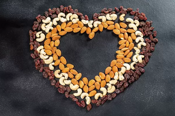 Heart lined from cashew nuts, almonds and raisins on a black background. Top view (Flip 2019)