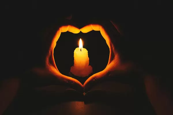 Heart-shaped hands and flame candle in darkness