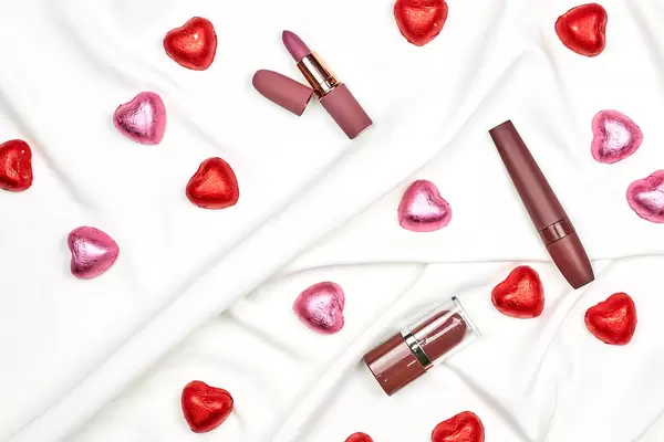 Heartshape chocolate candies and feminine lipsticks on white