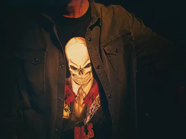 Heavy Metal Fan trägt Jeanshemd und Shirt mit großem Totenkopfmotiv und steht im Dunkeln