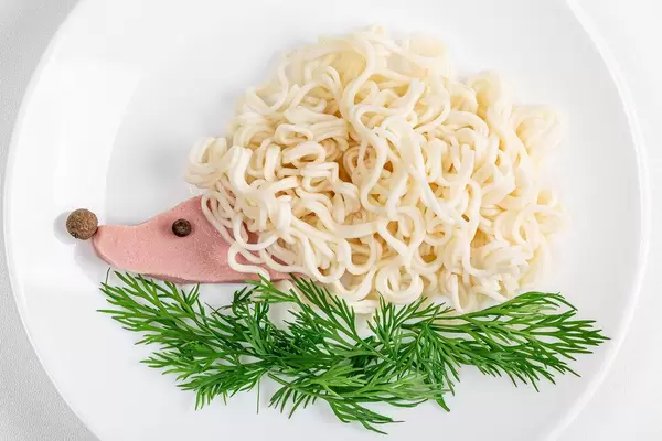Hedgehog made from macaroni and sausage with green dill on a plate