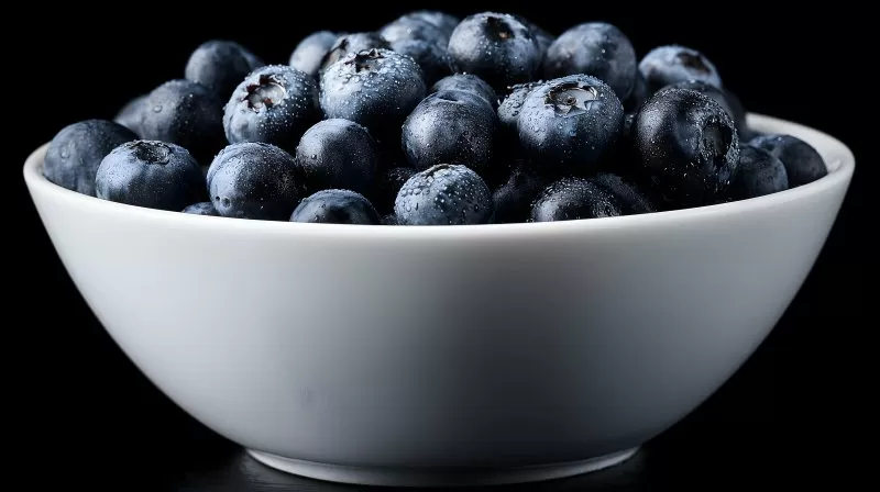 Heidelbeeren in weißer Schüssel vor schwarzem Hintergrund