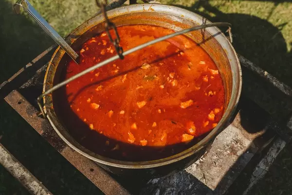 Heiße Tomatensuppe mit Fleisch in einem rustikalen Topf über einer Feuerstelle