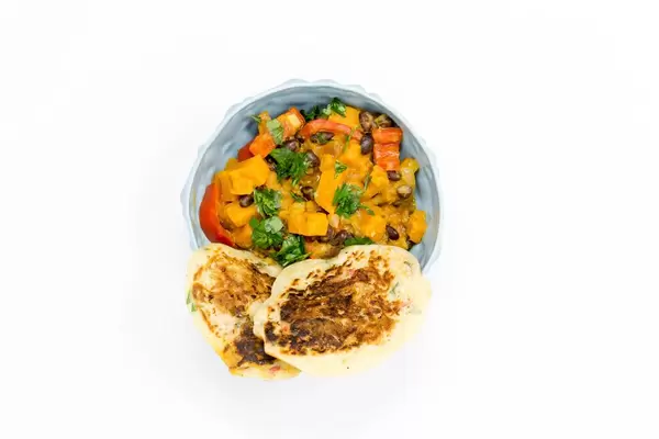 Hello Fresh - Carribian Sweet Potato Coconut Stew with Black Beans and Tasty Bananapancakes in blue bowl on white background - Top view